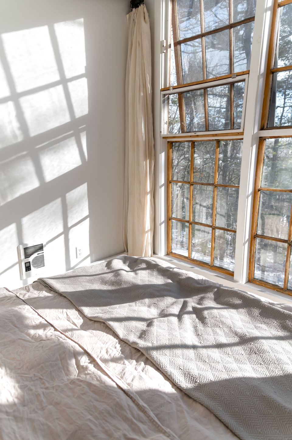 Chambre baignée de soleil, linge blanc et grandes fenêtres à petits carreaux