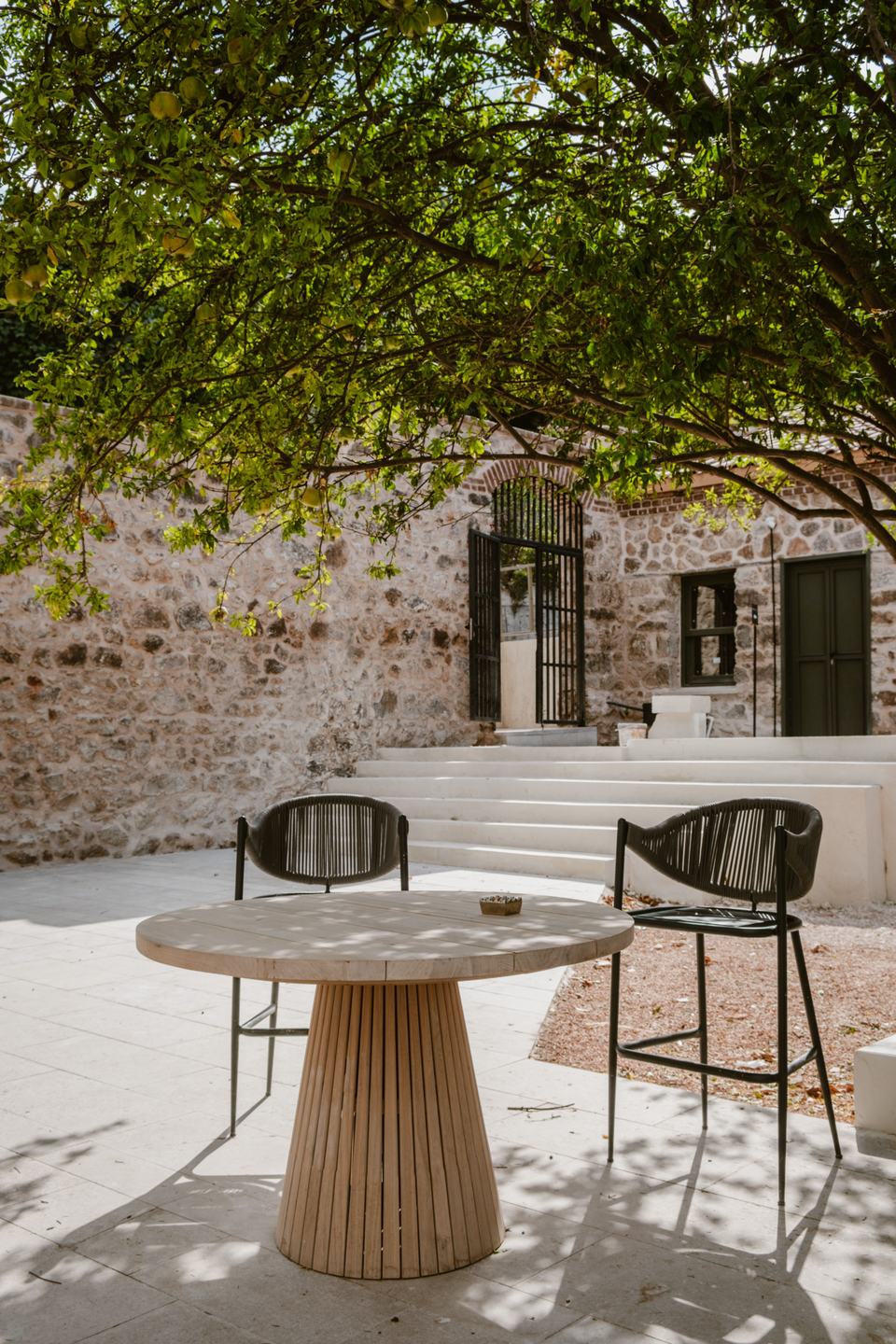 Cour de pierre à l’ombre d’un arbre, table ronde en bois et deux chaises