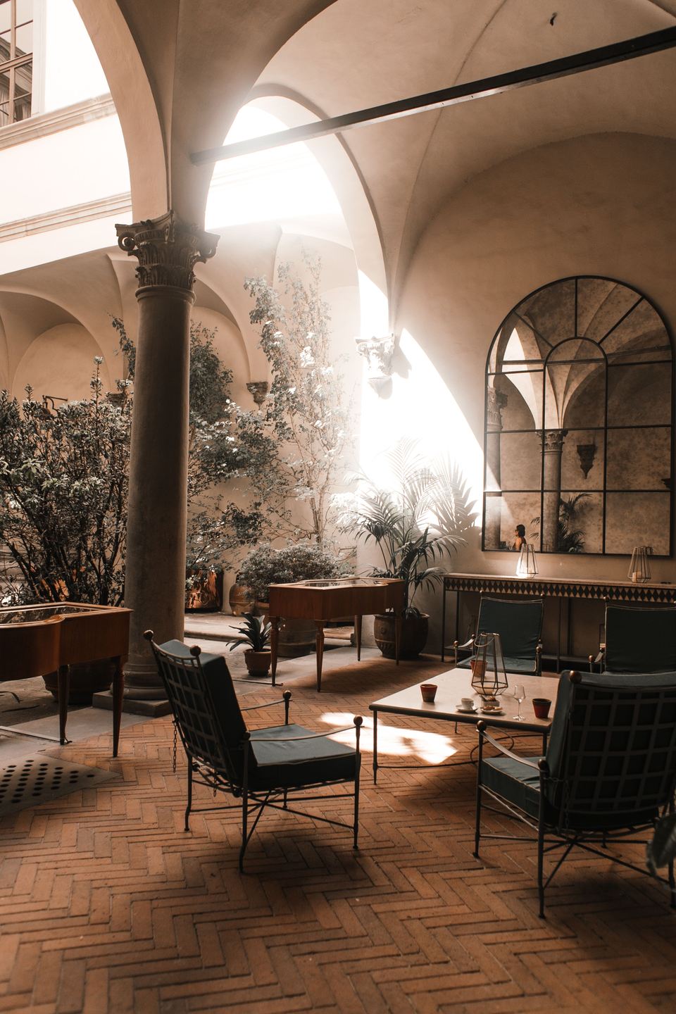 Salon sous des voûtes claires, colonnes, fauteuils de fer et sol de brique en chevrons