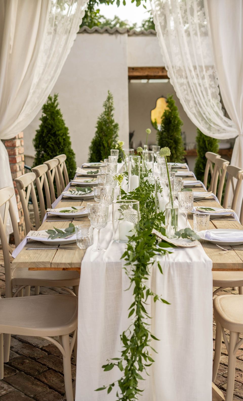 Longue table dressée sous des voilages, chemin de lin et verdure