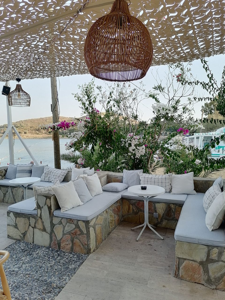 Terrasse sous une toile ajourée, banquettes de pierre, coussins clairs et suspension en osier