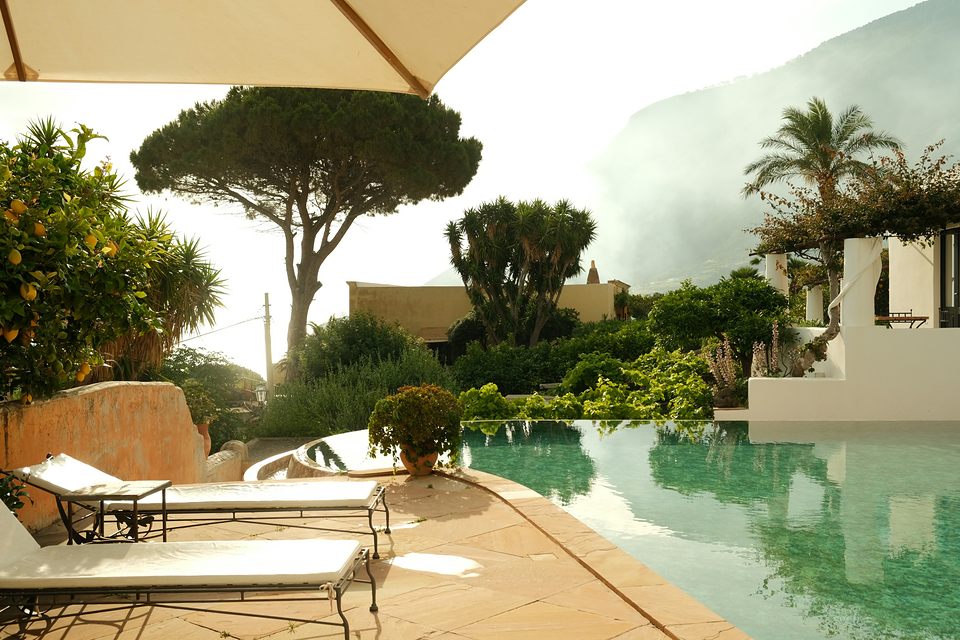 Piscine à débordement, bains de soleil à matelas clairs sous un parasol, pin parasol et palmiers