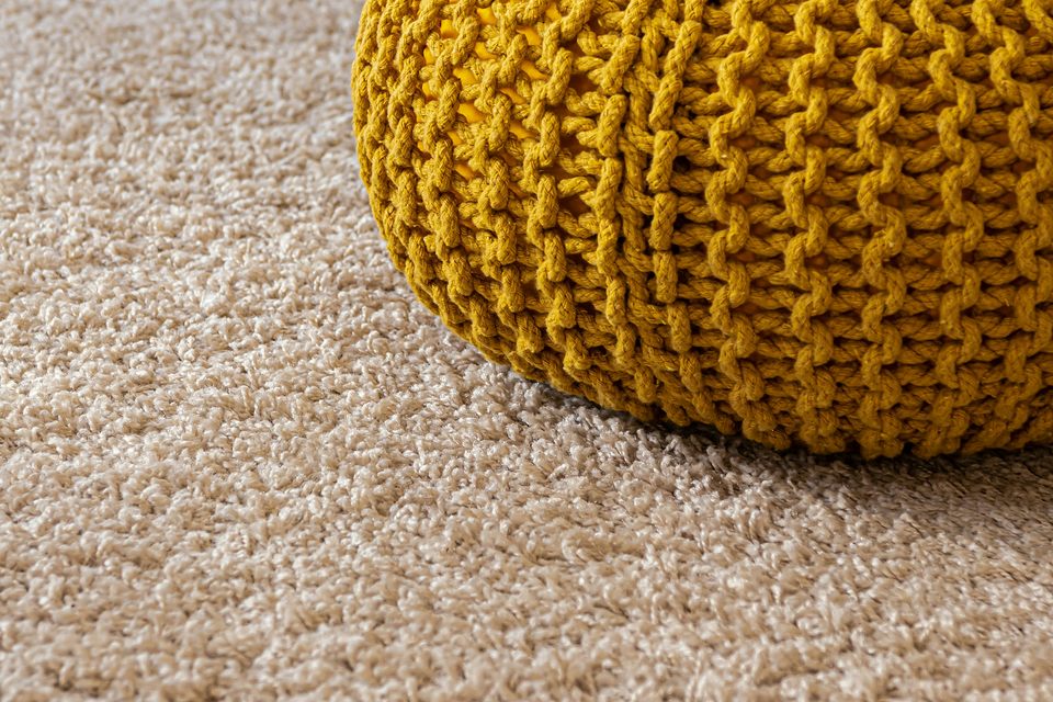 Moquette beige en gros plan, pouf tricoté posé dessus