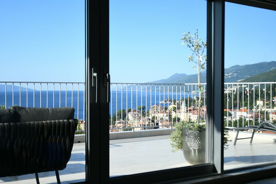 Baie vitrée coulissante ouverte sur une terrasse, la mer et la côte au fond